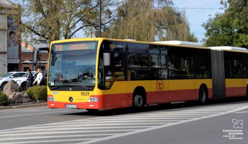 Ulica, po której jedzie czerwono-pomarańczowy autobus komunikacji miejskiej. Nad jego przednią szybą wyświetla się napis: 710 Konstancin-Jeziorna.
