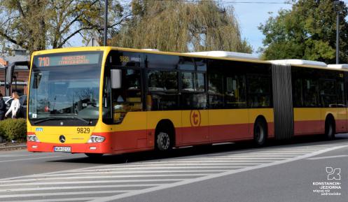 Ulica, po której jedzie czerwono-pomarańczowy autobus komunikacji miejskiej. Nad jego przednią szybą wyświetla się napis: 710.