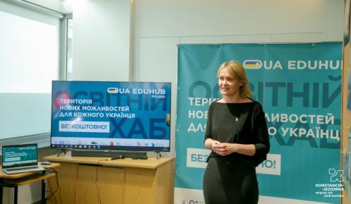 Osoba stoi i opowiada, w tle tablica oraz monitor