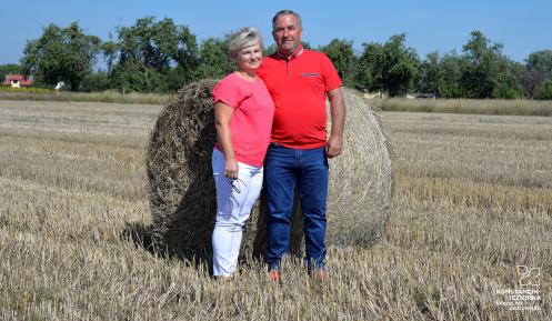 Kobieta i mężczyzna stoją na skoszonym polu, w tle bele słomy.