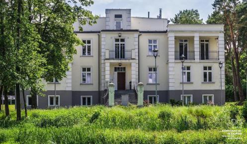 Budynek jednokondygnacyjny, zabytkowy w otoczeniu parkowych drzew.