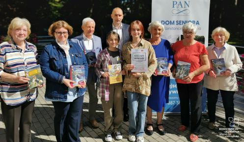 Grupa osób, młodszych i starszych, trzyma w ręku książkę „Ballady i romanse”.