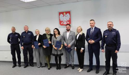 Na zdjęciu pracownicy GOSIR  i trzech policjantów, którzy stoją na tle białęj ściany z herbem Polski