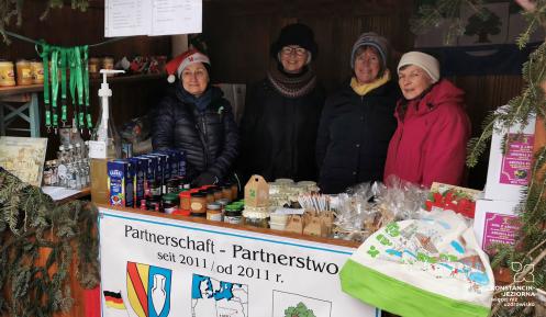 Zdjęcie stoiska z herbem Konstancina-Jeziorny, Za lada cztery kobiety. Na ladzie artykuły spożywcze.