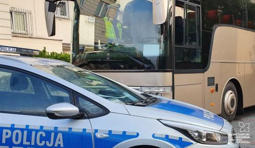 Radiowóz policyjny, obok niego stoi autokar