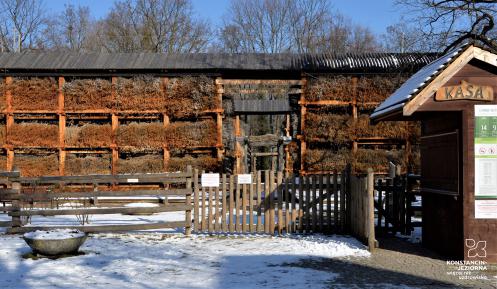 Tężnia, na pierwszym planie drewaniany budyneczek kasy, nad tężnią błękitne niebo.