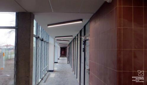 Długi korytarz w budynku szkoły, z lewej wysokie okna.