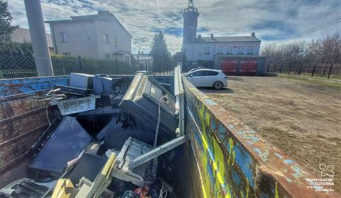 Na zdjęciu w pierszym planie kontener wypełniony elekroodpadami, w głębi bydynki strażnicy Ochorniczej StrażyPożarnej w Skolimowie.