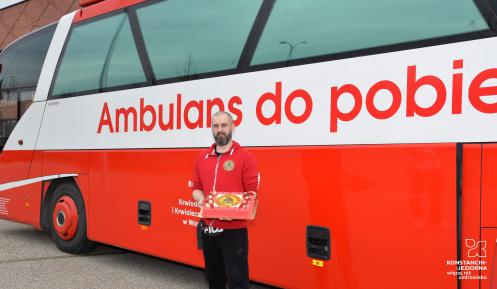 Mężczyzna trzymający tort przed czerwonym autobusem.