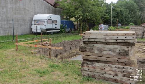 Plac budowy, na pierwszym planie materiały budowlane, w tle fragment wykopu. 