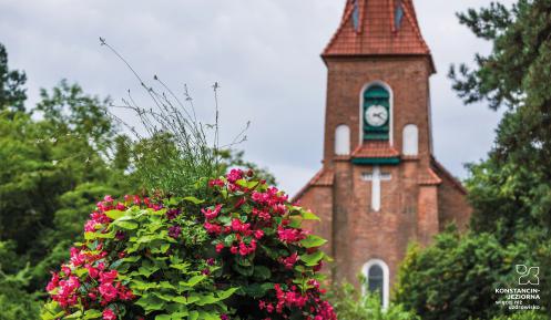 Na pierwszym planie donica z kwiatami, dalej fragment budynku kościoła z czerwonej cegły