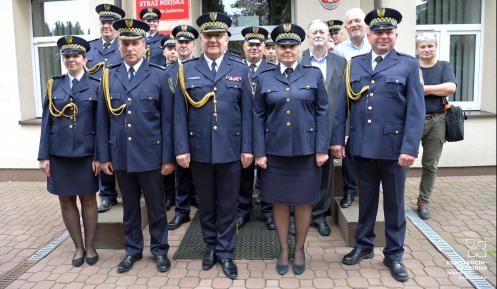 Na tle budynku stoi grupa mężczyzn i kobiet, ubranych w mundury straży miejskiej.