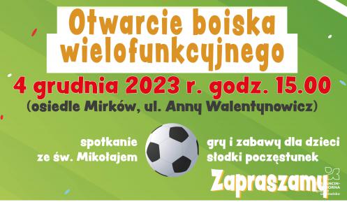 Grafika przedstawia plakat informujący o otwarciu boiska wielofunkcyjnego. Tłem jest zielona murawa, a w pierwszym planie znajdują się nożyce przecinające czerwoną wstęgę.