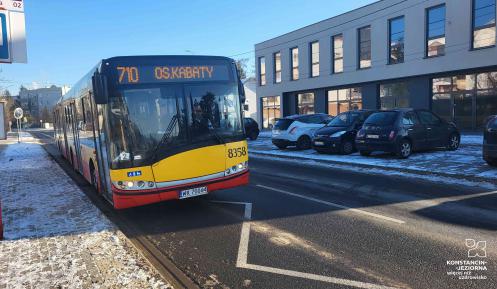 Ulica, po której jedzie czerwono-pomarańczowy autobus komunikacji miejskiej.