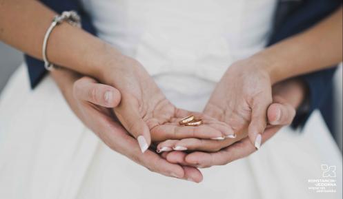 Nowożeńcy: dłonie meżczyzny podtrzymują od spodu dłonie kobiety. Kobieta w dłoniach trzeba obrączki.