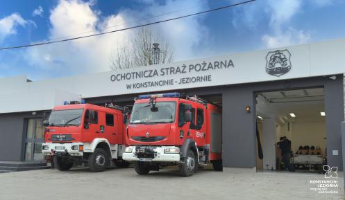 Dwa wozy strażackie, stojące przed dużym odnowionym budynkiem Ochotniczej Straży Pożarnej w Konstancinie-Jeziornie. 
