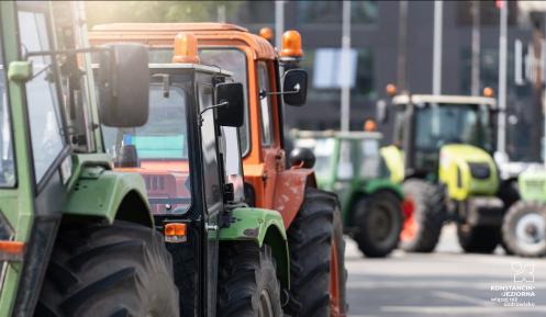 Na ulicy stoją ustawione w rzędzie traktory.