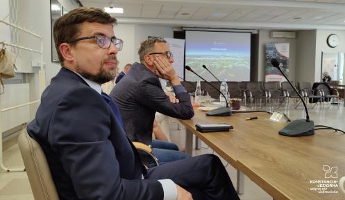 Mężczyzna w garniturze i w okularach siedzi za stołem w sali konferencyjnej