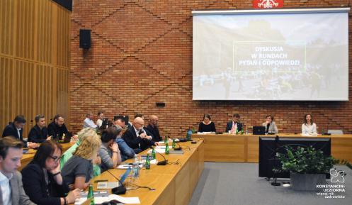 Grupa osób siedzi przy stole w sali posiedzeń.