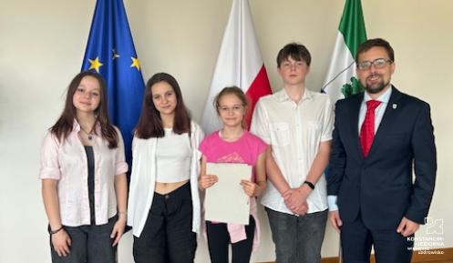 Czterech uczniów i mężczyzna w garniturze stoją obok siebie. 