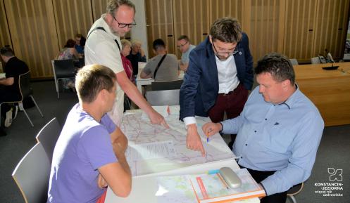Kilka osób patrzy na mapę tras autobusowych leżącą na stoliku
