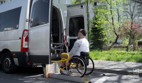 Osoba na wózku inwalidzkim, przed samochodem transportowym 