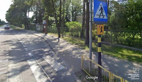 Fragment ulicy z chodnikiem, w tle przystanek autobusowy