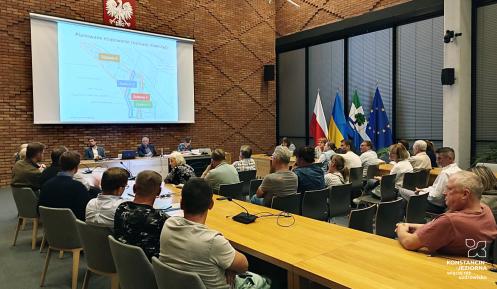 Spotkanie w sali posiedzeń, ludzie siedzą na krzesłach.