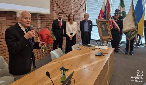 Starszy mężczyzna trzyma w rękach mikrofon i kwiaty.