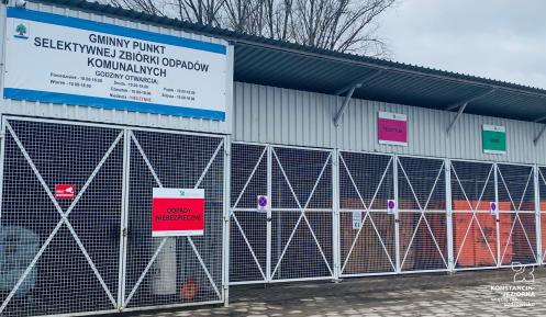 Na zdjęciu metalowa podłużna wiata. Pod nią stoi sześć dużych kontenerów budowlanych. Na wiacie powieszony jest duży baner z napisem: Gminny Punkt Selektywnej Zbiórki Odpadów Komunalnych.