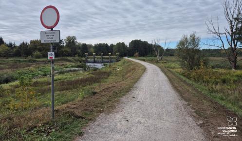 Droga polna, w tle drzewa i jaz spiętrzający wodę.