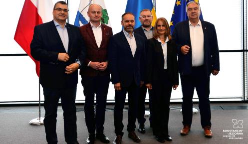 Grupa osób ubrana w garnitury na tle flag.