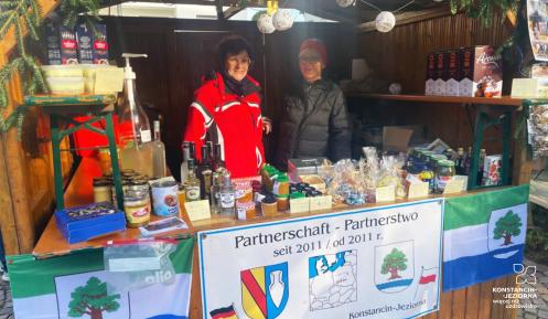  Stoisko świąteczne przedstawiające współpracę między Denzlingen a Konstancin-Jeziorna, ozdobione flagami oraz produktami lokalnymi.