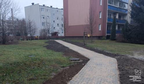 Nowo wyłożony chodnik z kostki brukowej otoczony terenem zielonym i blokami mieszkalnymi w zimowej scenerii.
