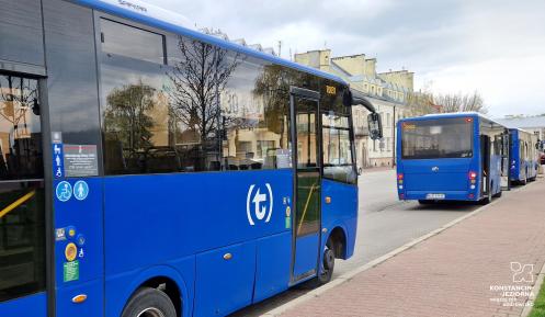 Trzy niebieskie autobusy miejskie stoją zaparkowane na przystanku wzdłuż chodnika przy ulicy.