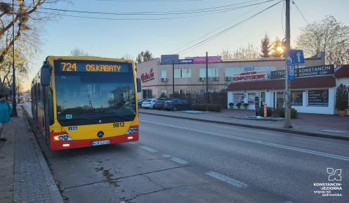 Autobus linii 724 z napisem OS. KABATY stojący na ulicy w pobliżu punktów usługowych i sklepów.