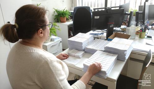 Kobieta siedzi przy biurku i pakuje listy do koperty. 