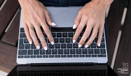 Kobieta z pomalowanymi na biało paznokciami pracuje na laptopie, trzymając dłonie na klawiaturze.