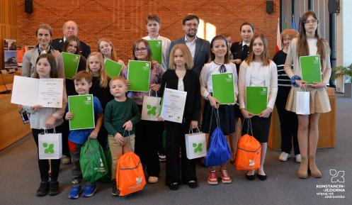 Grupa dzieci z dyplomami i kolorowymi plecakami.