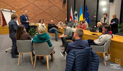 Grupa ludzi siedzi obok siebie z zeszytami i długopisami w ręku