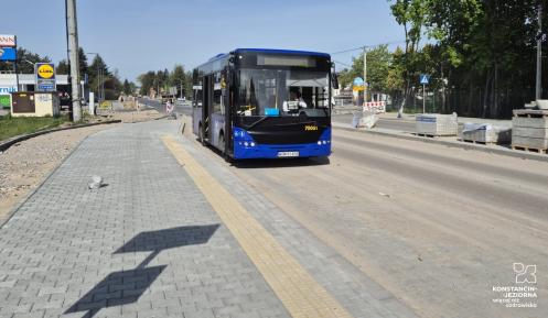 Niebieski autobus jadący ulicą w pobliżu sklepu Lidl, na tle trwających prac drogowych i świeżo ułożonego chodnika.