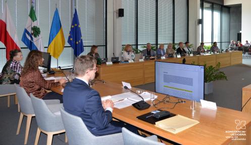 Grupa osób siedzi za stołami na sali posiedzeń.