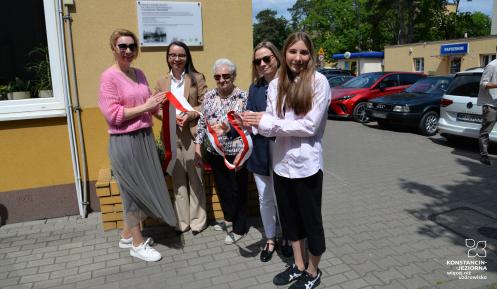 Pięć kobiet, w tym uczennica i seniorka, trzyma wstęgę podczas uroczystego odsłonięcia tablicy pamiątkowej na budynku przy ul. Jana Sobieskiego 6 w Konstancinie-Jeziornie.