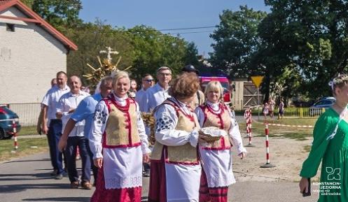 Kolorowy korowód dożynkowy z udziałem mieszkańców w tradycyjnych strojach ludowych i dziewcząt niosących wieniec z kłosów zbóż podczas święta plonów.
