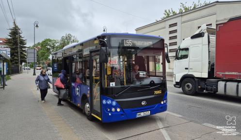 Niebieski autobus stoi na przystanku, w tle ulica z samochodami.