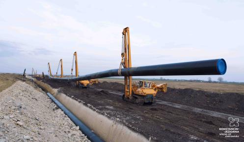 Ciężkie maszyny budowlane przenoszą i umieszczają rury gazociągowe w ziemi.