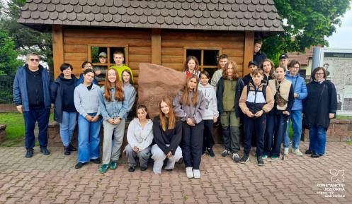 wycieczka szkolna, przed drewnianym budynkiem i kamiennym pomnikiem