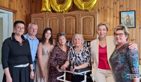 Rodzinne zdjęcie - grupa osób stoi, w środku solenizantka. Nad nimi złoty balon - liczba 100.