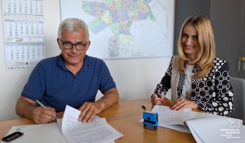 Kobieta i mężczyzna siedzą przy stole i podpisują dokumenty.