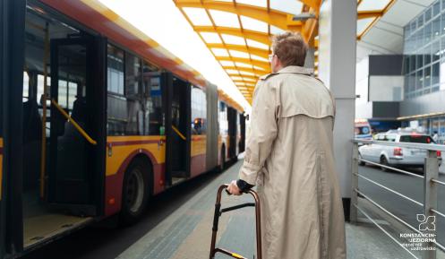 Kobieta stoi na przystanku autobusowym i chce wsiąść do pojazdu.